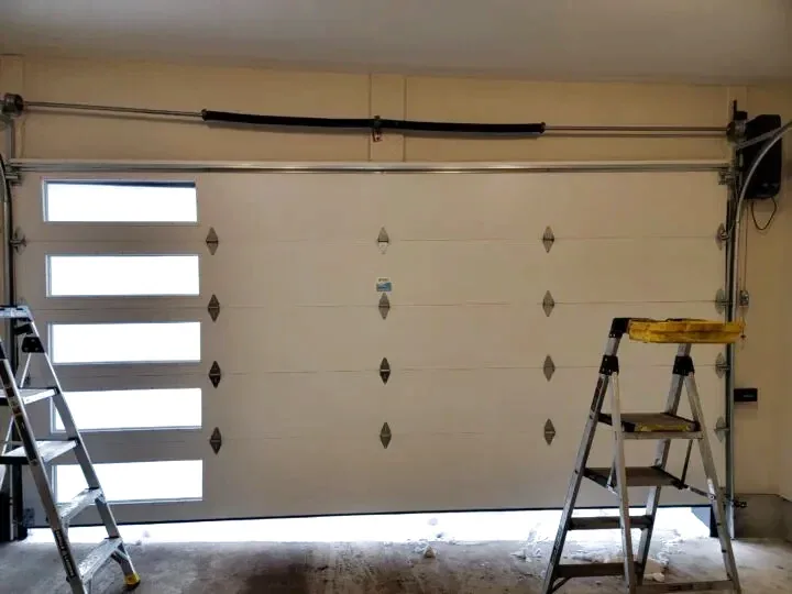Interior view of a residential garage door showing the lift cables, drums, and torsion bar after a fresh install